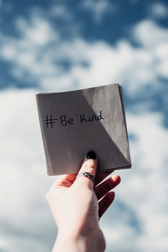 portfolio-05 A hand holding a note with #Be kind inscribed, set against a bright sky.